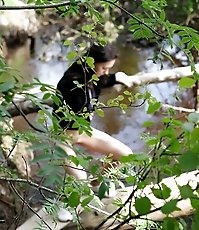 Teenage brunette peeing into a river in the park