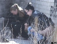 Two girls relieve themselves behind a building